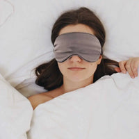 Frau trägt Graue Schlaf-Seidenmaske im Bett für erholsamen Schlaf